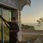 A friendly, uniformed professional providing trusted residential window cleaning services for a sunny home in Gibraltar, showcasing a crystal-clear view of the Mediterranean.