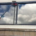 A professional window cleaner using a pure-water Reach & Wash pole system to safely clean high-level glass on a sunny day in Gibraltar.