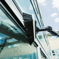 Cleaning operative using a telescopic Reach and Wash water-fed pole system to safely clean high-rise windows from the ground.
