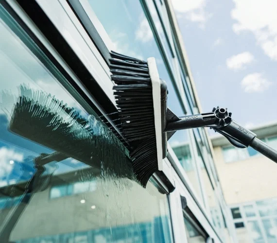 Cleaning operative using a telescopic Reach and Wash water-fed pole system to safely clean high-rise windows from the ground.