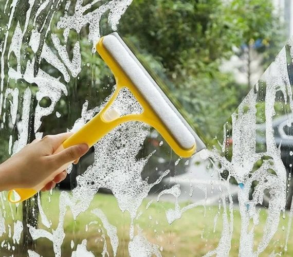Close-up of a Reach & Wash window cleaning brush head actively scrubbing UPVC window frames, sills, and exterior glass with 100% purified water.
